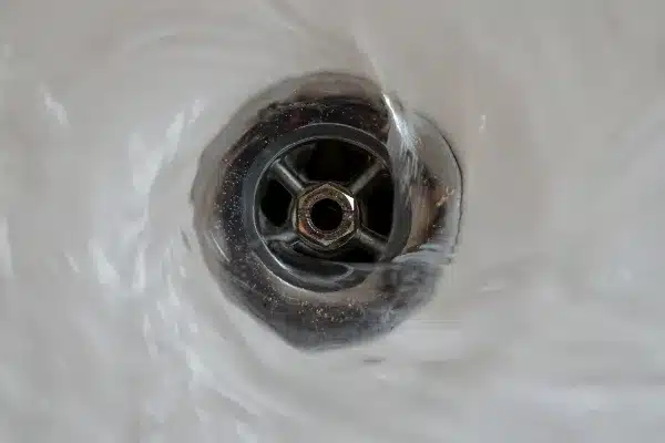 Close-up of water swirling down a metallic drain, creating a vortex-like pattern reminiscent of expert rooter services in action.