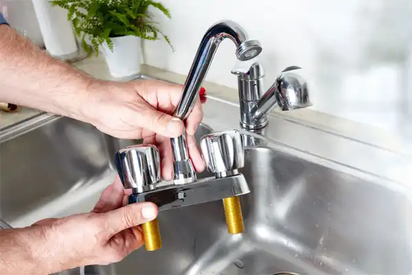 A person is holding a detached kitchen faucet above a stainless steel sink.